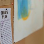 Close-up of a corkboard with a to-do list and colorful artwork in an office setting.